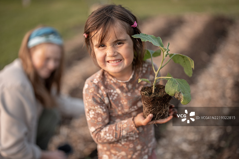 微笑的女孩在柔和绿色背景的花园中抱着一株植物图片素材