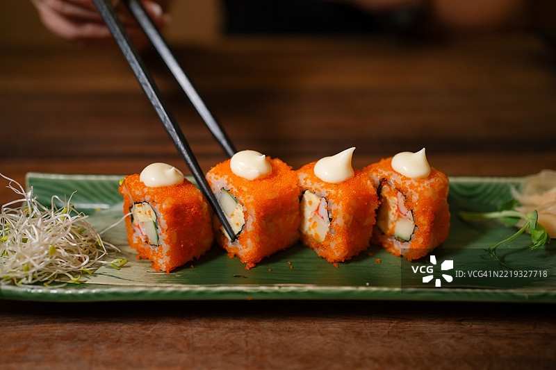 筷子从寿司盘中夹起一块寿司卷。图片素材