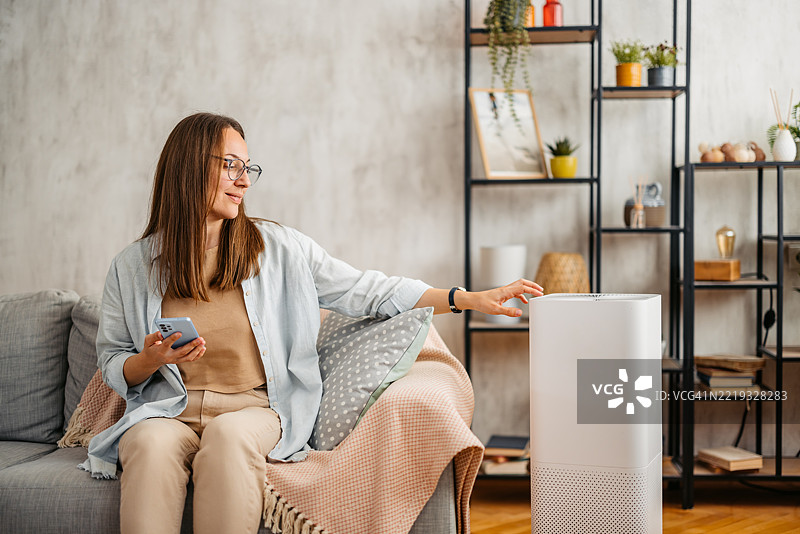 年轻女性在家沙发上用手机开启空气净化器图片素材
