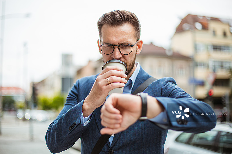 商人在城市街道上喝咖啡并查看手表时间图片素材