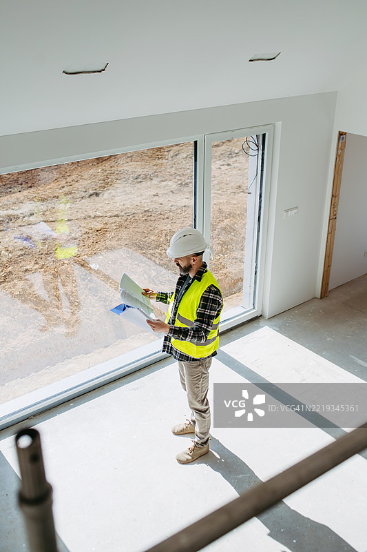 高角度视图的建筑工人在工地上检查建筑计划。图片素材