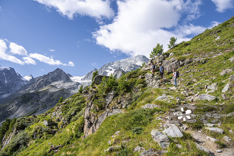 三名登山者在徒步旅行小径上，背景是阿罗拉附近的山脉，蒙科隆峰和特西乔尔新冰川，瓦莱州，西阿尔卑斯，瑞士，欧洲图片素材