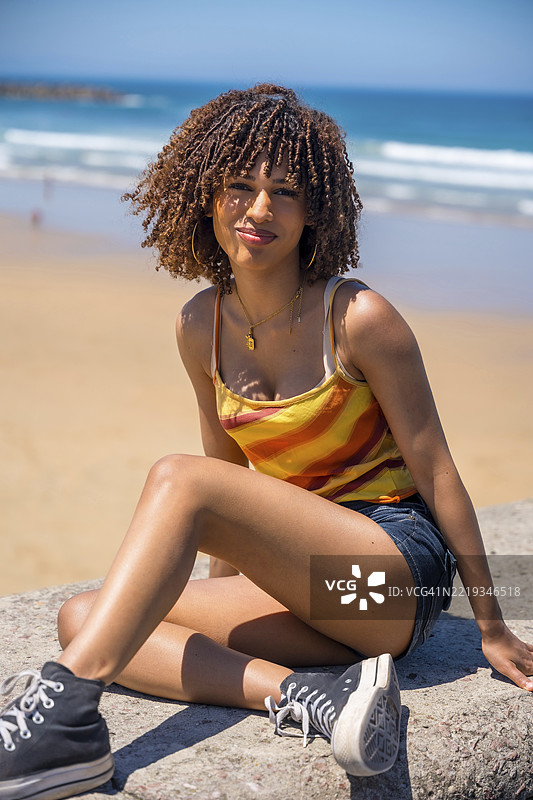 年轻女子坐在海滩墙上，享受阳光明媚的天气和海洋景色图片素材