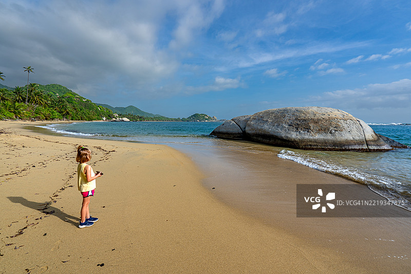 年轻女孩在哥伦比亚南美洲的泰罗纳国家公园美丽的拉皮斯基纳海滩上玩耍，背景是加勒比海和圣玛尔塔山脉。图片素材