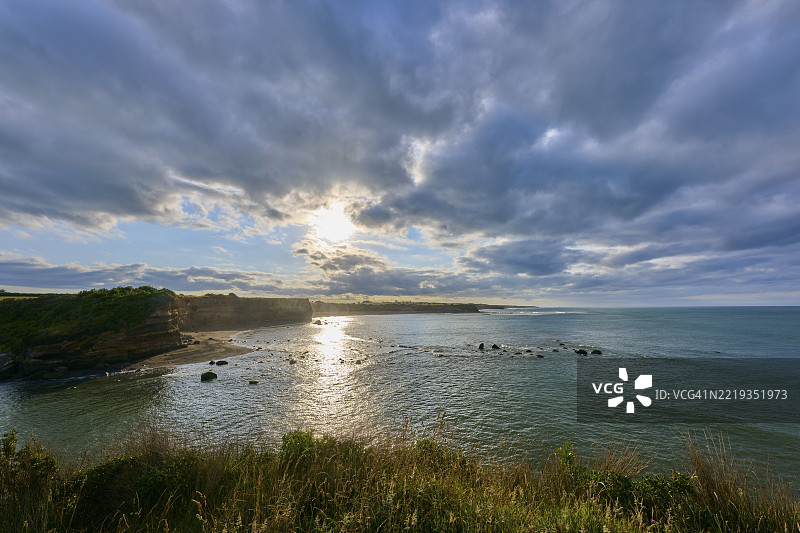 新西兰北岛塔拉纳基地区奥普纳基的平静海面上的日出，戏剧性的云彩和光线反射图片素材