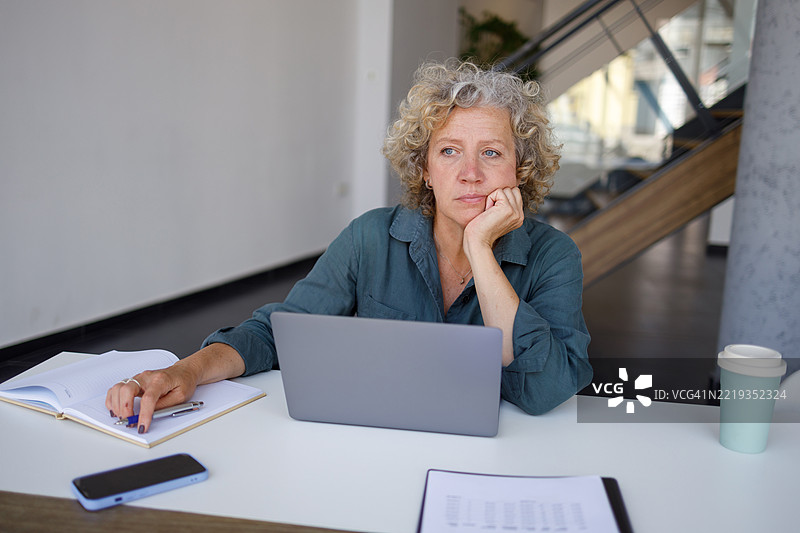 成熟的女商人在办公桌前使用笔记本电脑，沉思着她在商业上的下一步行动。图片素材
