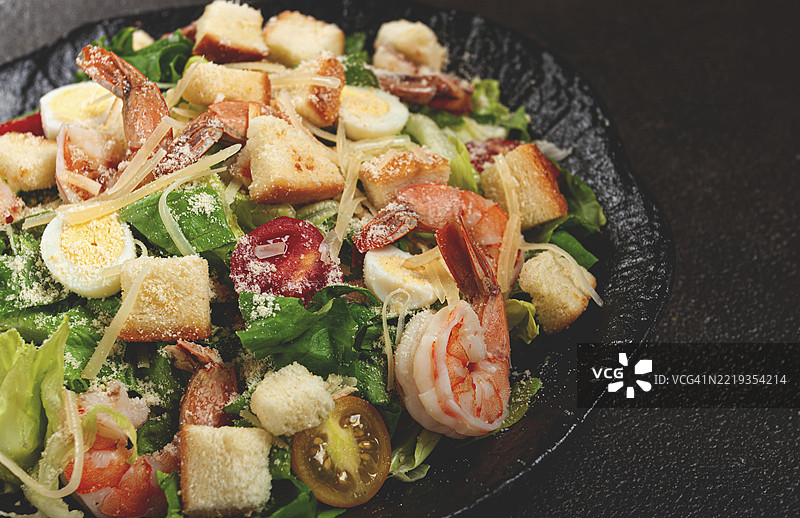 黑盘上的凯撒沙拉，配有老虎虾、虾沙拉、生菜叶、鹌鹑蛋、樱桃番茄和帕尔马干酪图片素材