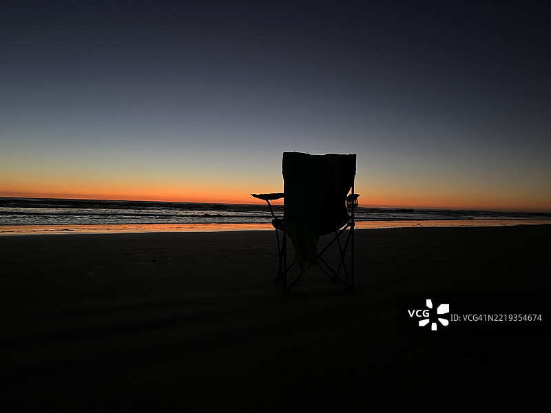 沙滩上被橙色晨光照亮的休闲椅剪影图片素材