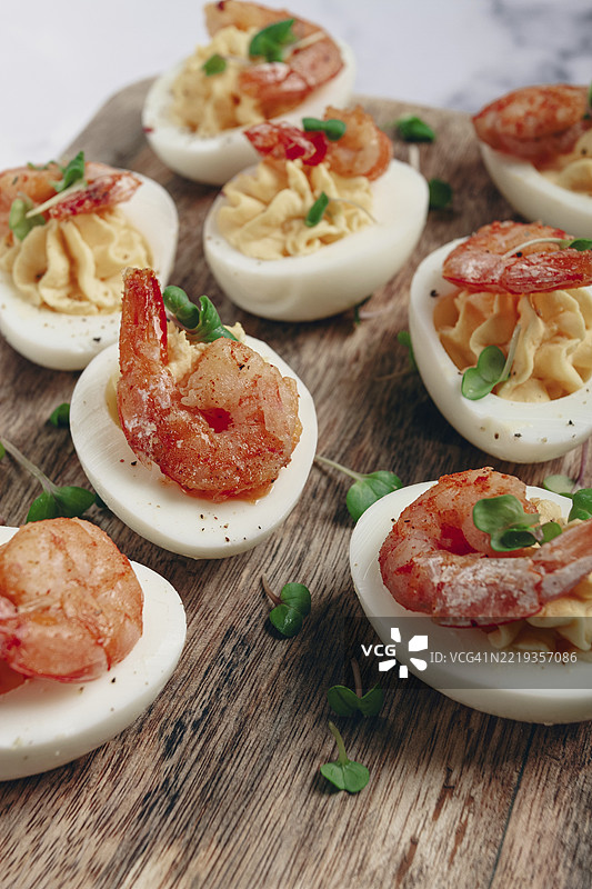 用蛋黄和蛋黄酱调味的煮鸡蛋，虾仁填充的鸡蛋，放在木砧板上，特写，聚焦，没人。图片素材