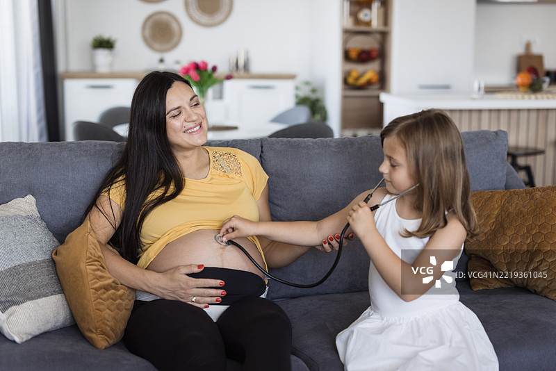 女孩在给怀孕的妈妈扮演医生。图片素材