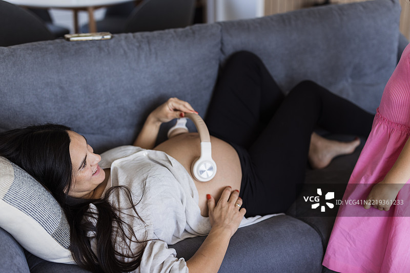 孕妇在休息时将无线耳机放在肚子上。图片素材