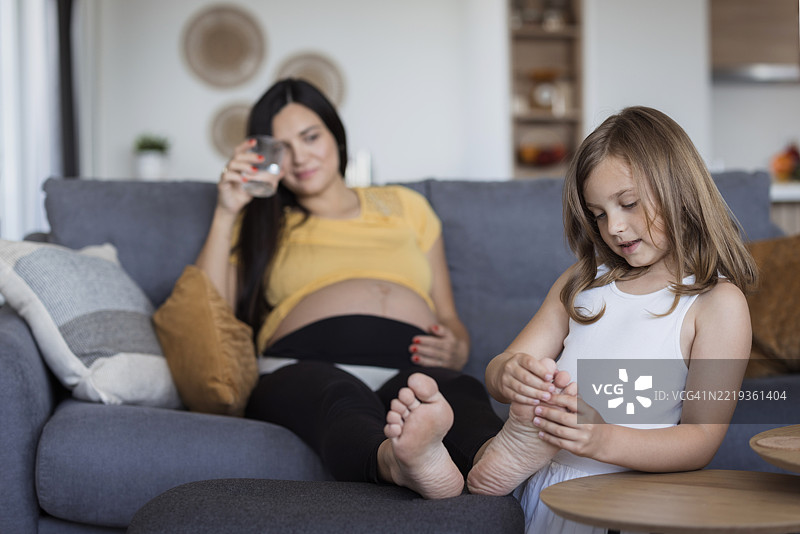 快乐的女孩为怀孕的妈妈按摩脚部图片素材