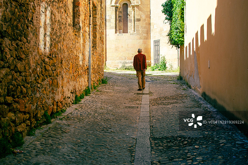 孤独的老年男子在古老的城镇小巷中走开图片素材
