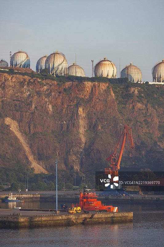 工业景观，港口起重机和储罐位于岩石面前，西班牙比斯开省希洪，欧洲图片素材