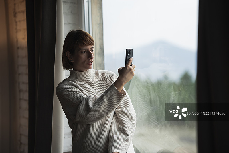 女人用智能手机拍摄窗外的风景图片素材