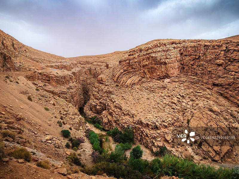 沿着著名的达德斯峡谷蜿蜒而上的空旷山路,周围是植物和陡峭深邃的沉积岩层,位于摩洛哥丁吉尔省的布马尔内达德斯(Boumalne-Dadès)。图片素材
