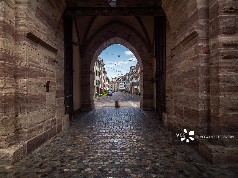 斯普兰门（Spalentor）下方的人行石板小道，这是巴塞尔昔日防御墙的一部分，通向一条有电车轨道和多彩建筑的街道，瑞士巴塞尔市。图片素材