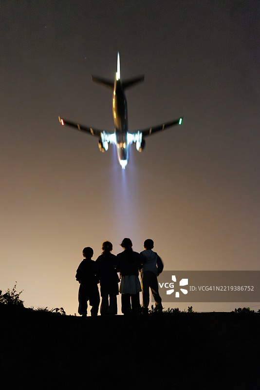 四个亚洲孩子在夜晚观看飞机降落的背影图片素材