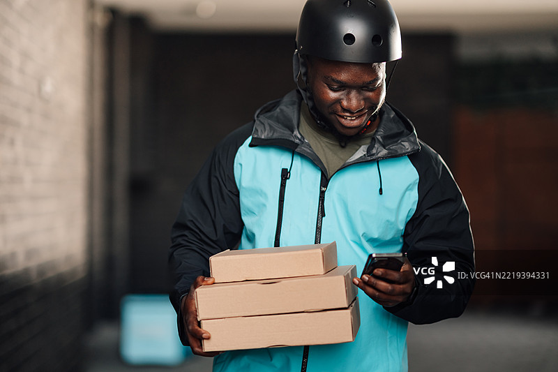 送餐员在查看智能手机上的地址，同时携带着比萨盒。图片素材