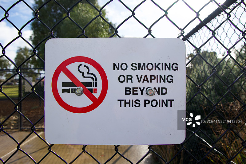 “此处禁止吸烟或电子烟”标志挂在公共公园入口的铁丝网围栏上图片素材
