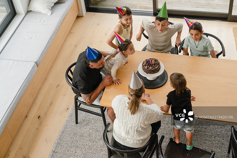 生日女孩在家人陪伴下许愿，吹灭蜡烛。图片素材