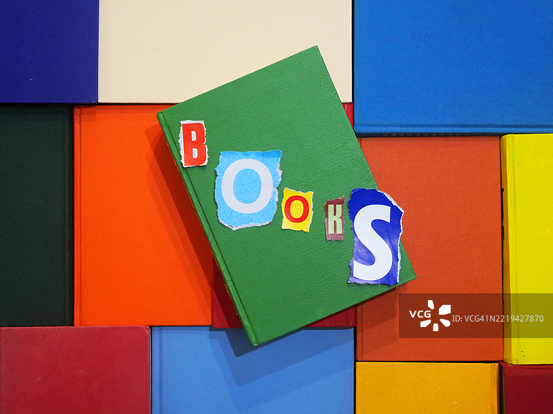 用不同颜色的字母写成的“书”字,撕下的纸张,放在书的封面上。阳光。自然色彩。法国巴黎。图片素材