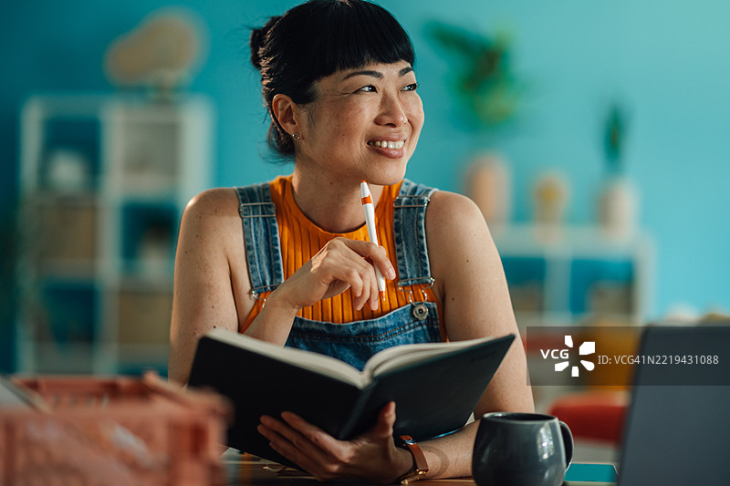 微笑的女性手持笔和笔记本，思考并望向远方图片素材