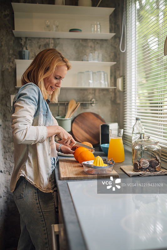 女人在现代厨房里切橙子，准备新鲜榨汁。图片素材