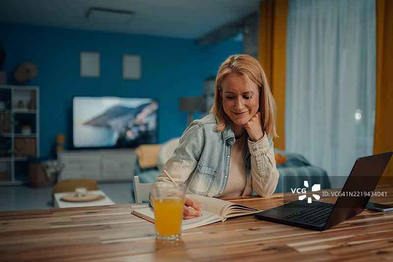 晚上在家工作的女性，边做笔记边微笑图片素材