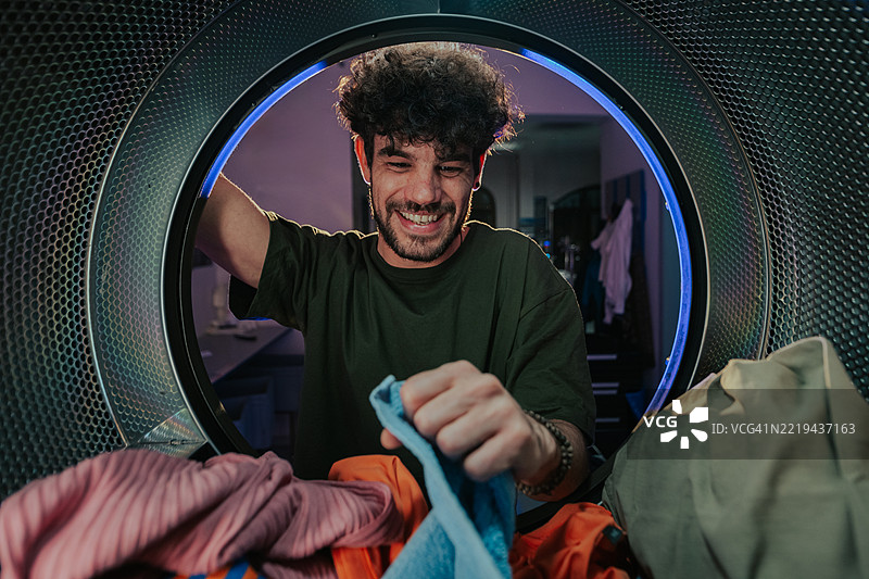 年轻男子在自助洗衣店将衣物放入大容量洗衣机中图片素材