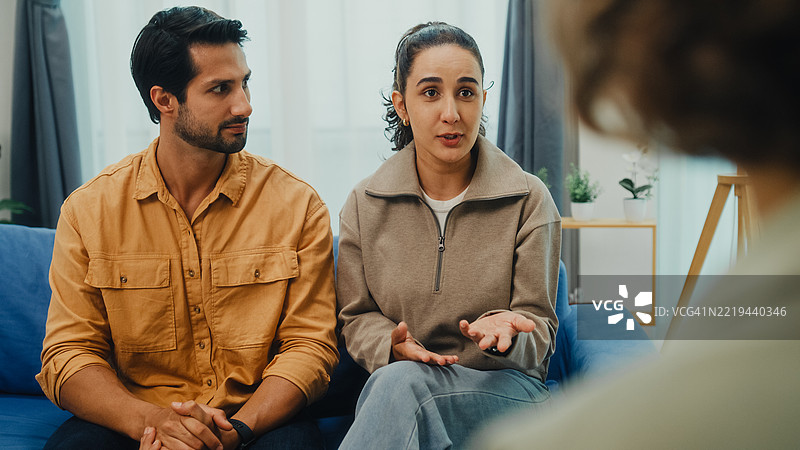 年轻夫妇在家中的客厅沙发上与心理健康专业人士进行严肃讨论，参加婚姻咨询会议。治疗会议心理健康概念。图片素材
