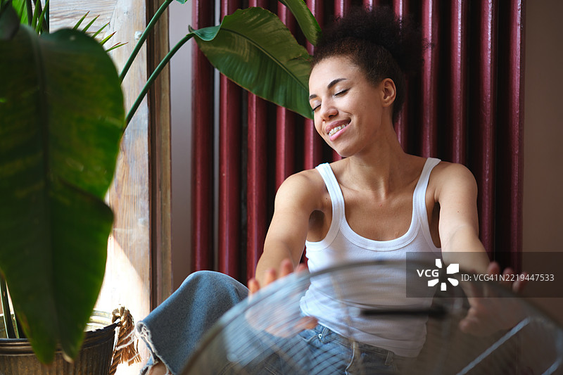 夏季炎热。快乐满足的年轻女性在炎热的夏天使用电风扇降温，在没有空调的公寓里度过热浪。图片素材