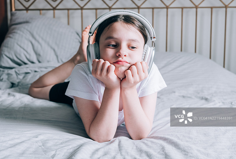 一个青春期前的女孩正在戴着耳机听音乐。图片素材