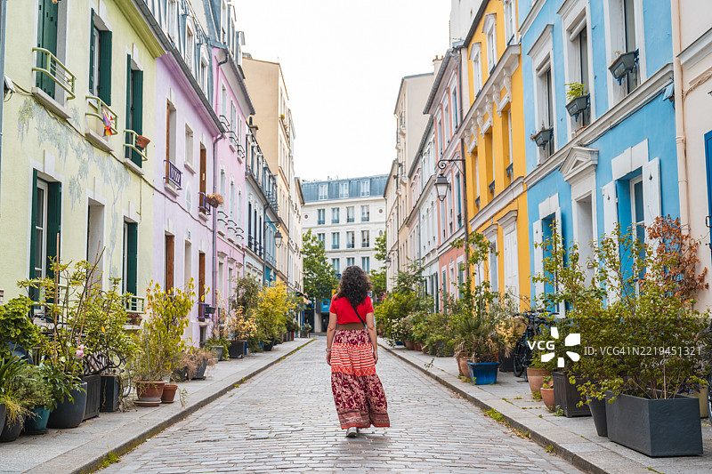 一位女性在法国巴黎的彩色房屋间走在鹅卵石街道上图片素材