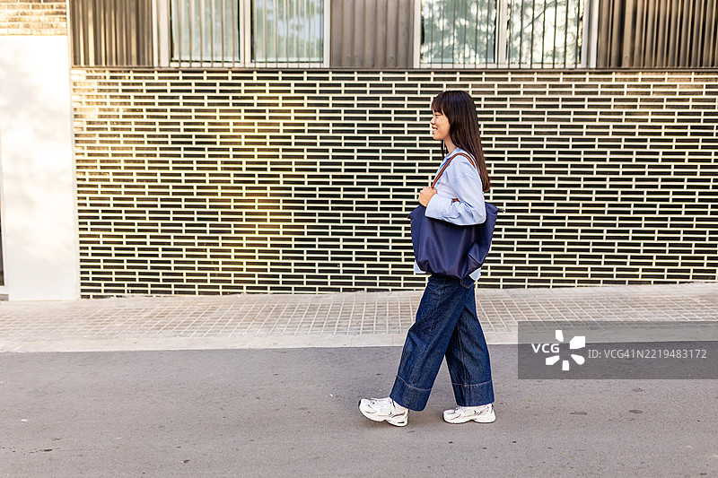 年轻的亚洲女性提着手提袋在街上行走图片素材