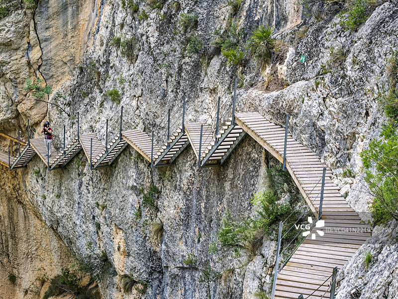 冒险旅游，一位女性沿着嵌入峡谷岩壁的木栈道行走。雷尤桥（Pasarela de Relleu）图片素材