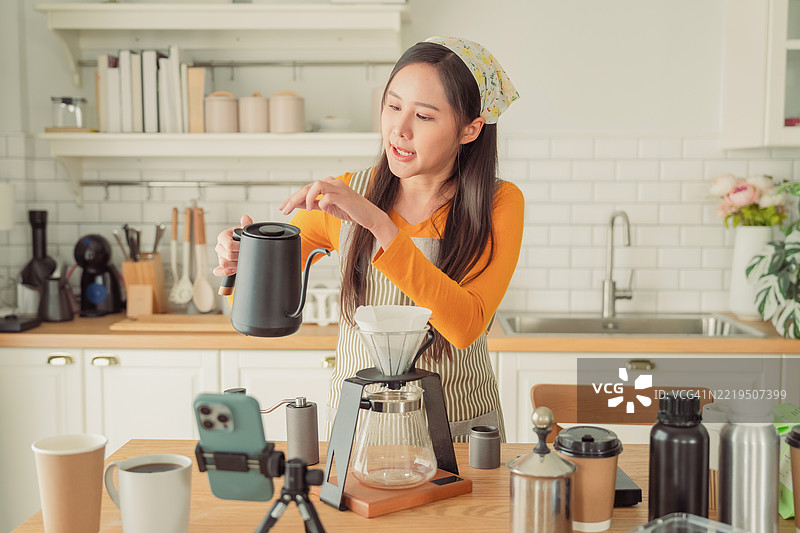 一位快乐的亚洲女咖啡师正在直播制作完美热浓咖啡的教程，分享专业技巧给咖啡爱好者，同时为她的社交媒体频道录制视频。场景设在一家现代咖啡馆，她的内容推广在线学习。图片素材