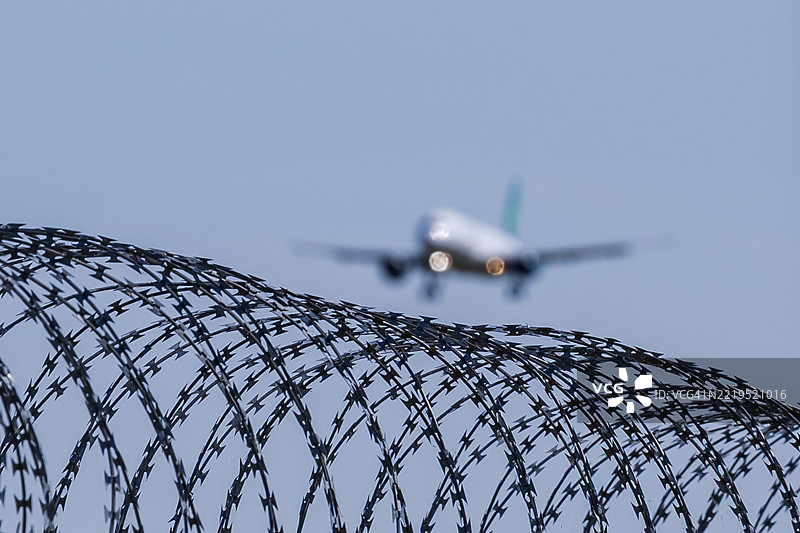 带刺铁丝网与空中接近的客机图片素材