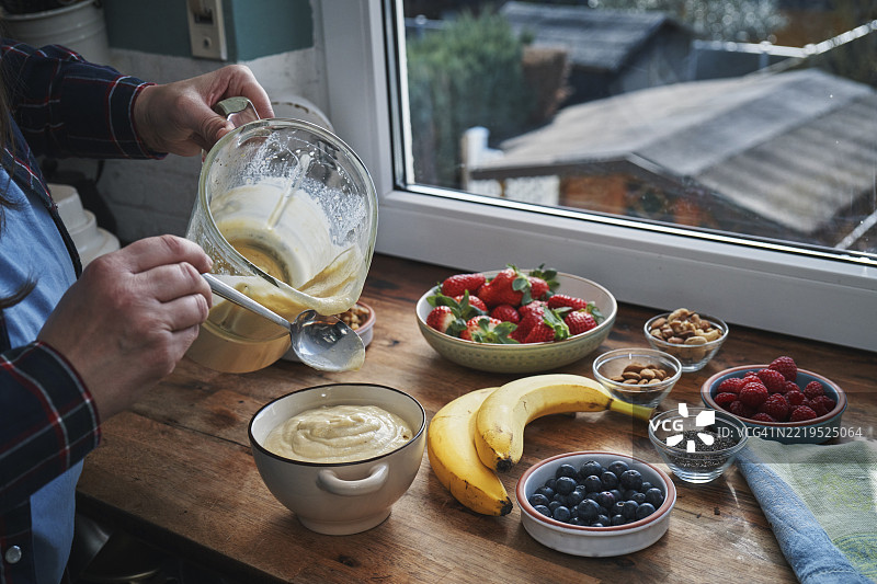 在乡村风格的木质厨房台面上准备健康的水果坚果种子冰沙，使用搅拌机。图片素材