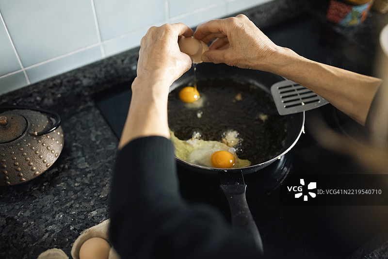 一位女性在家中的厨房为家人准备食物，正在平底锅中用橄榄油煎蛋。图片素材