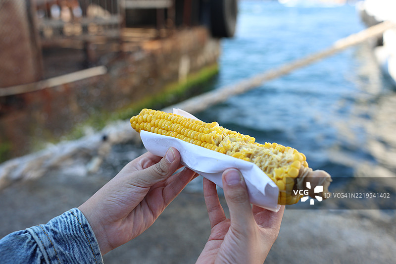 男人在海边手持玉米的特写镜头图片素材