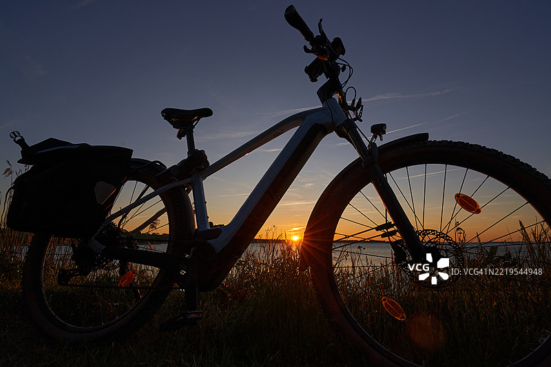 丹麦厄尔岛上，夕阳下海边的电动山地自行车剪影图片素材