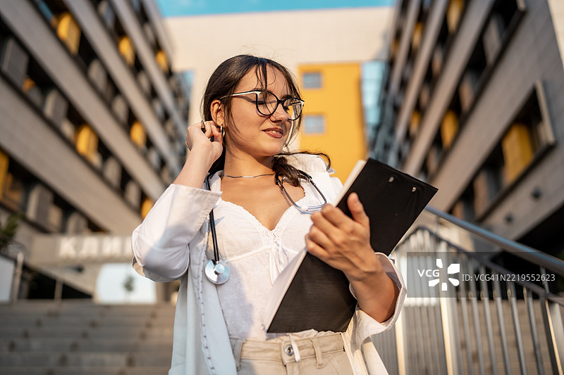 自信的女性医生在现代城市环境中手持夹板图片素材