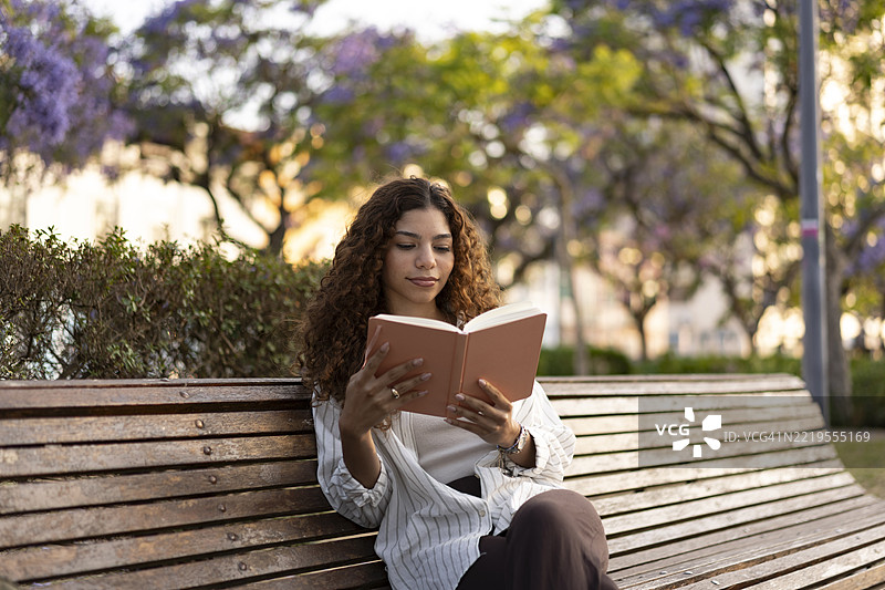 春天的公园长椅上，少女正在阅读一本书图片素材