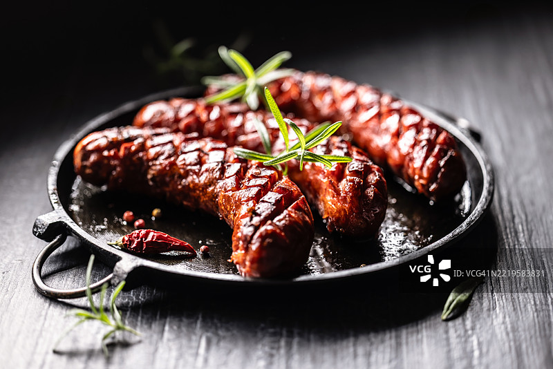 三根香肠在铸铁平底锅上烤至酥脆，点缀着一枝迷迭香图片素材