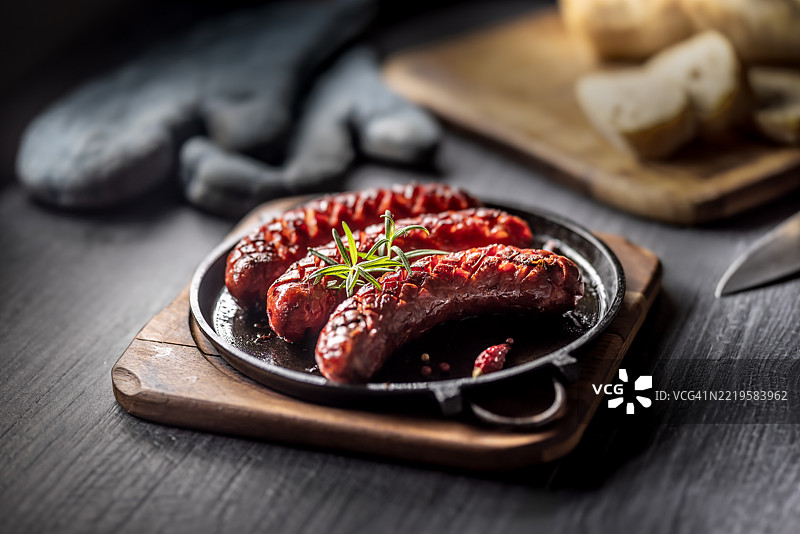 三根香肠在铸铁平底锅上烤至酥脆，点缀着一枝迷迭香图片素材