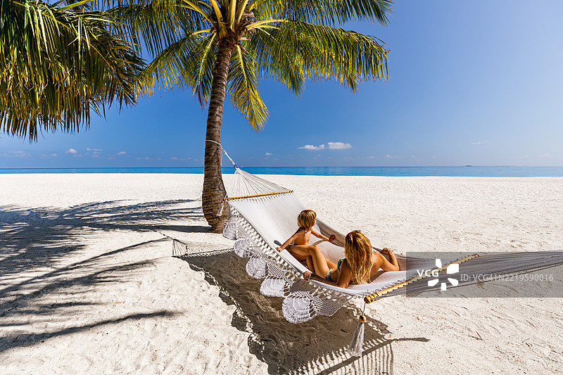 小男孩和他的单身母亲在海滩的吊床上放松。图片素材