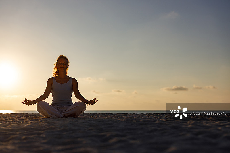 在日落时分，放松的女性在海滩上冥想。图片素材