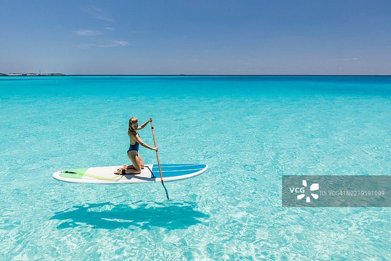 快乐的女人在夏日的海上享受划桨板的乐趣。图片素材