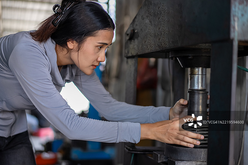 一位自信的年轻女性正在工厂里使用液压机修理摩托车零件。图片素材
